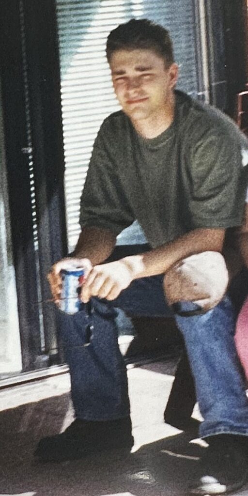 William in his early twenties, sitting outside, holding a Pepsi