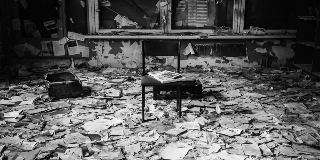 A chair in an abandoned building in a room with documents scattered all over the floor